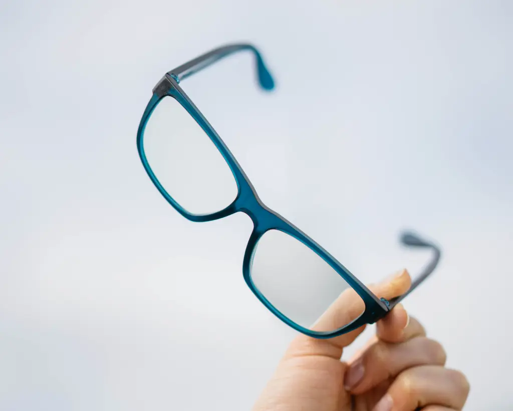 A hand holding modern blue-framed Dresden Vision prescription glasses against a light background, showing the frame's sleek design