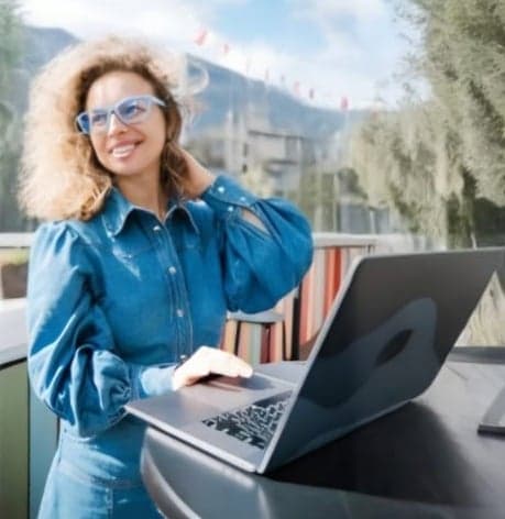 A professional woman in blue Dresden Vision New Zealand glasses enjoys an outdoor workspace, highlighting the perfect blend of eco-friendly design and modern style.