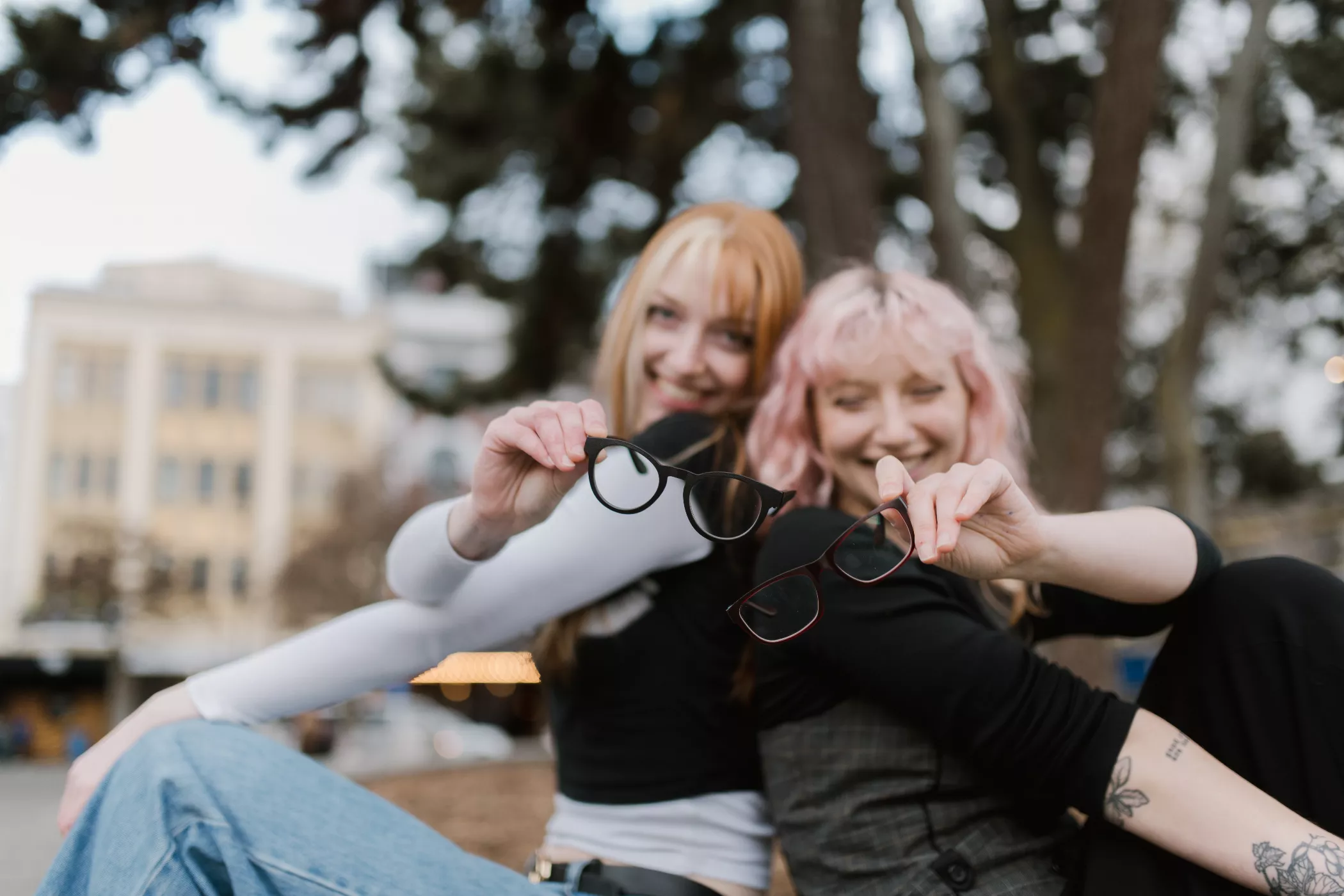 Two friends sharing a fun moment outdoors while holding up eco-friendly glasses fitted with Single Vision Lenses from Dresden Vision Australia, blending style with sustainability.
