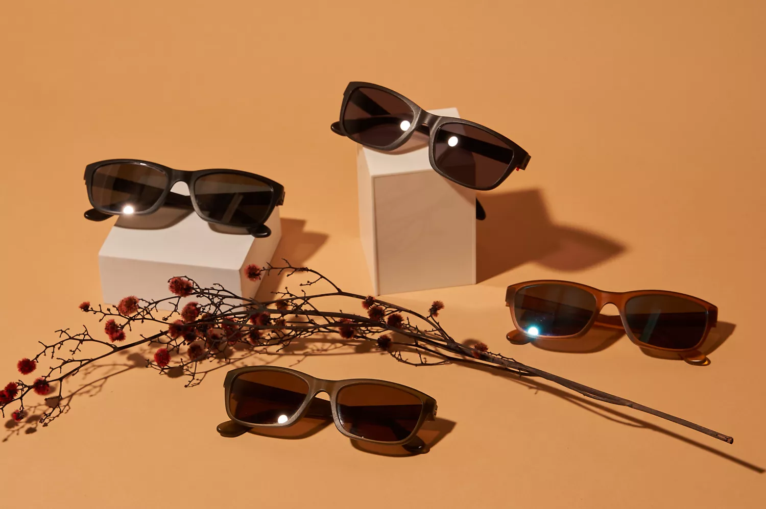 A color brown Dresden sunglasses having brown lenses. There a total of four Dresden sunglasses, having two placed on top of a box, and the other two placed on the ground. In between those Dresden glasses is some kind of flower.